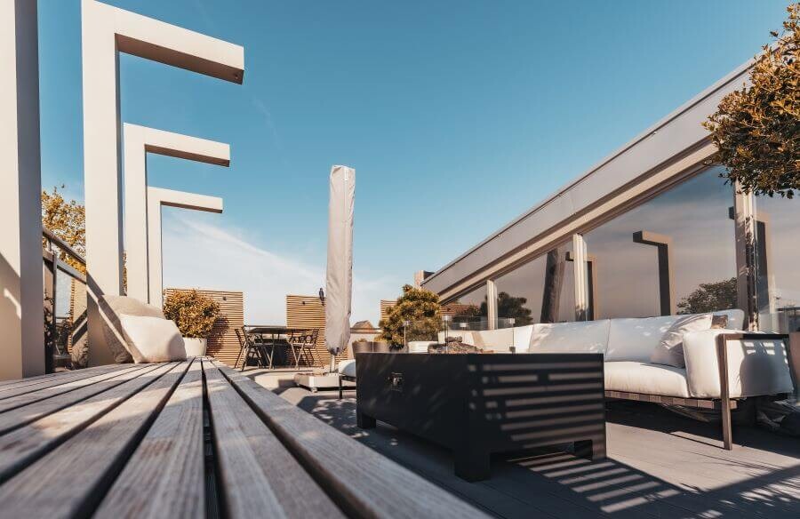Modern dakterras ontwerp lounge set vuurtafel houten bank stalen elementen pergola parasol dining tafel houten vloer planten potten (1)