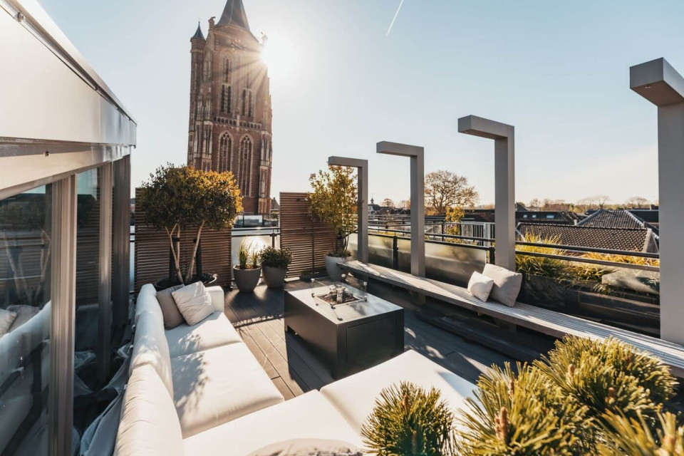 Modern dakterras ontwerp lounge set vuurtafel houten bank stalen elementen pergola planten potten meerstammigebomen siergrassen sfeer idee (1)