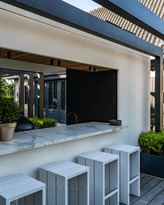 Buitenbar met witte krukken, marmeren aanrecht en potplanten. Modern ontwerp met bovenliggende balkenstructuur